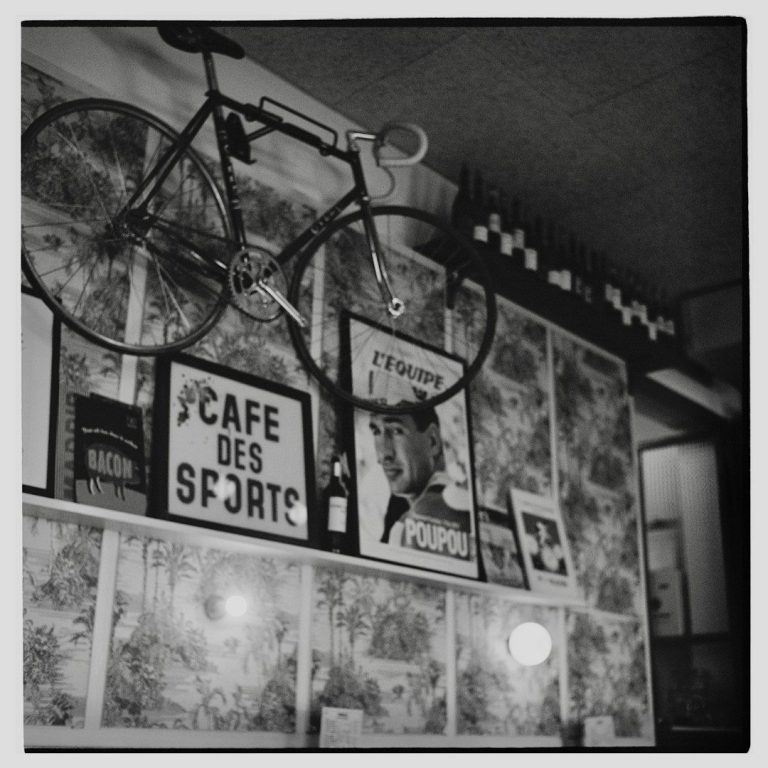 Werkstatt 7 Wanddekoration mit einem Fahrrad und mehreren gerahmten Plakaten in Schwarz-Weiß.